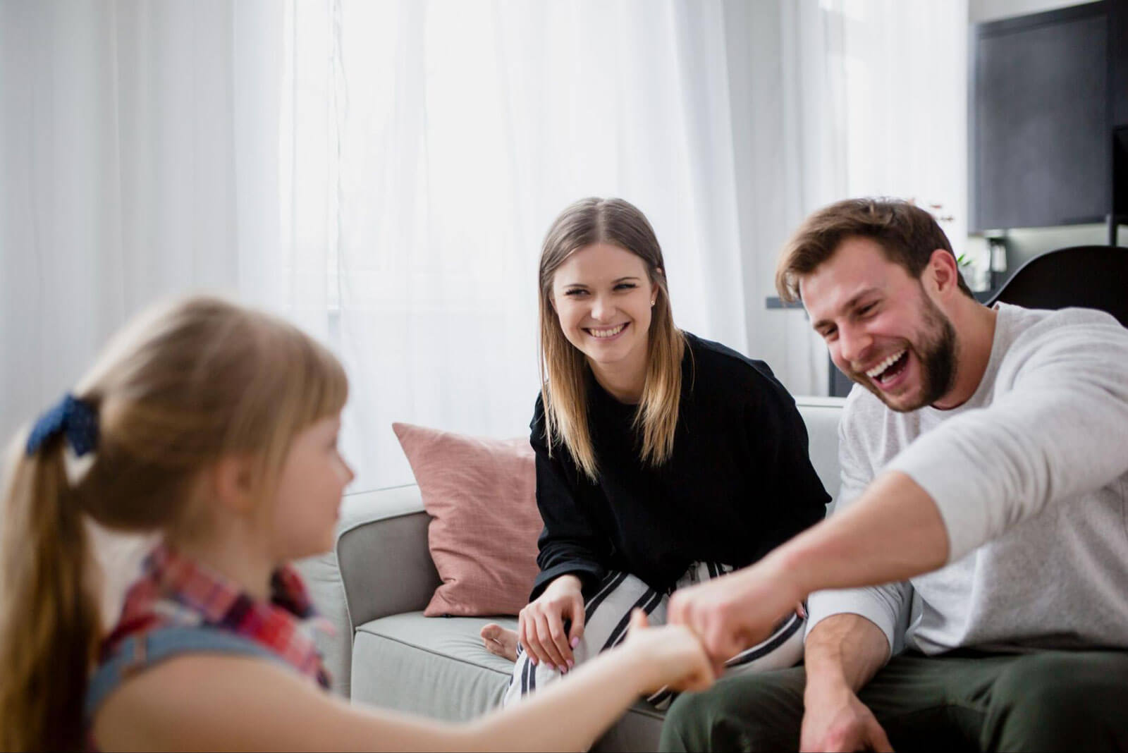 Parents and their child smiling and interacting together on a couch, representing connection, trust, and healing through family therapy.