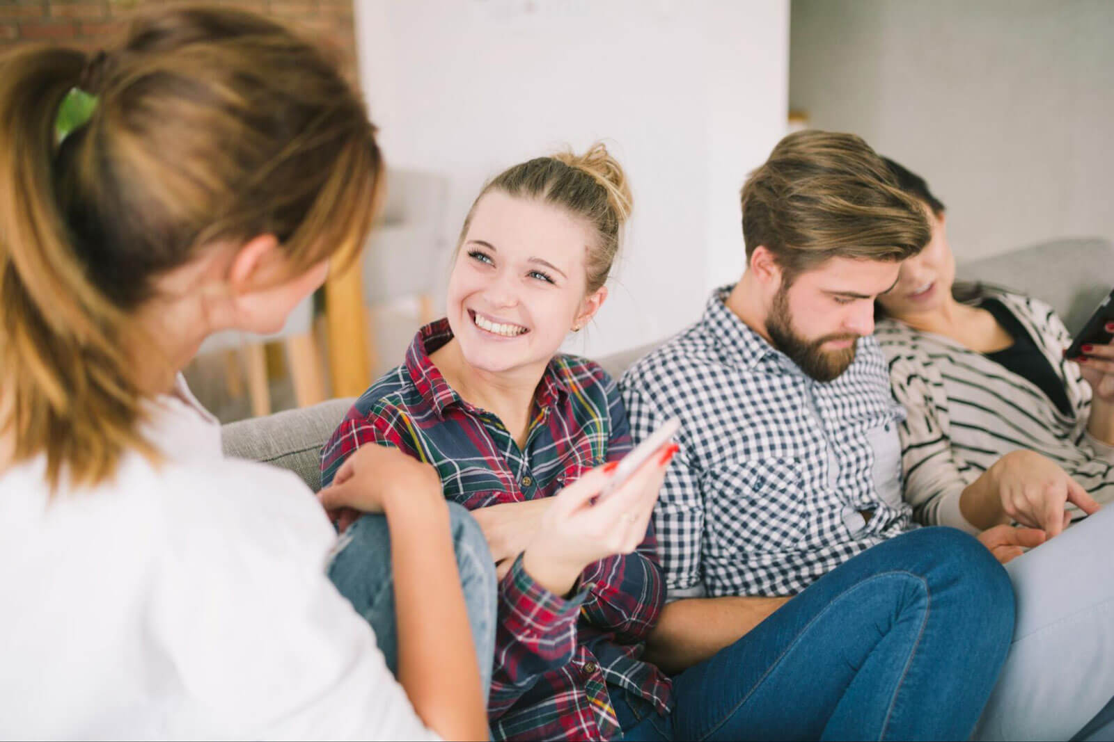 A smiling teen girl talks with an adult woman while other teens sit nearby looking at their phones.